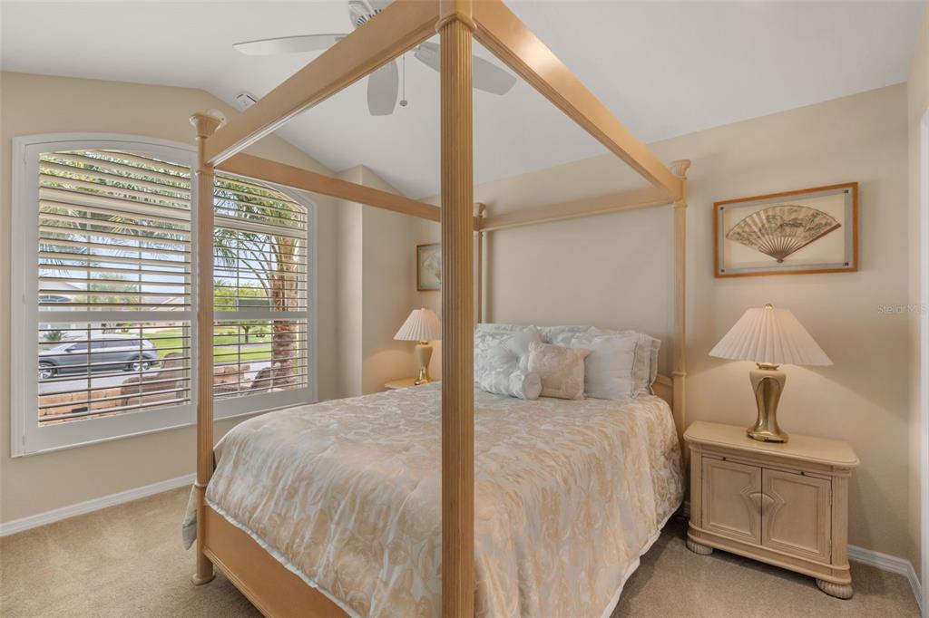 A bedroom features a wooden four-poster bed, nightstands with lamps, and windows with plantation shutters — 2643 JUPITER WAY, THE VILLAGES, FL