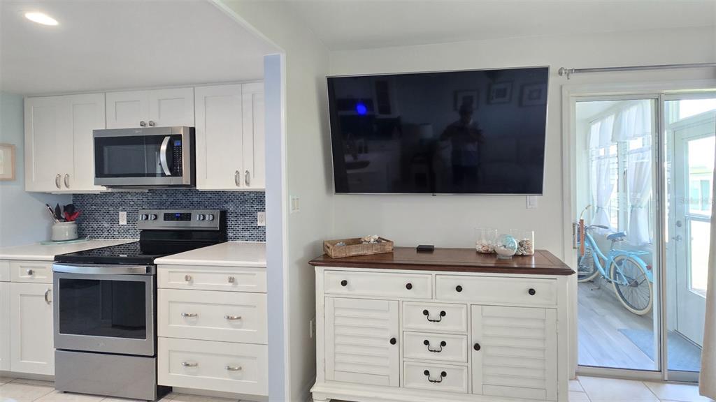 A kitchen with white cabinets and a blue tiled backsplash sits beside a living area — 608 BEACH PARK LANE UNIT V257, CAPE CANAVERAL, FL