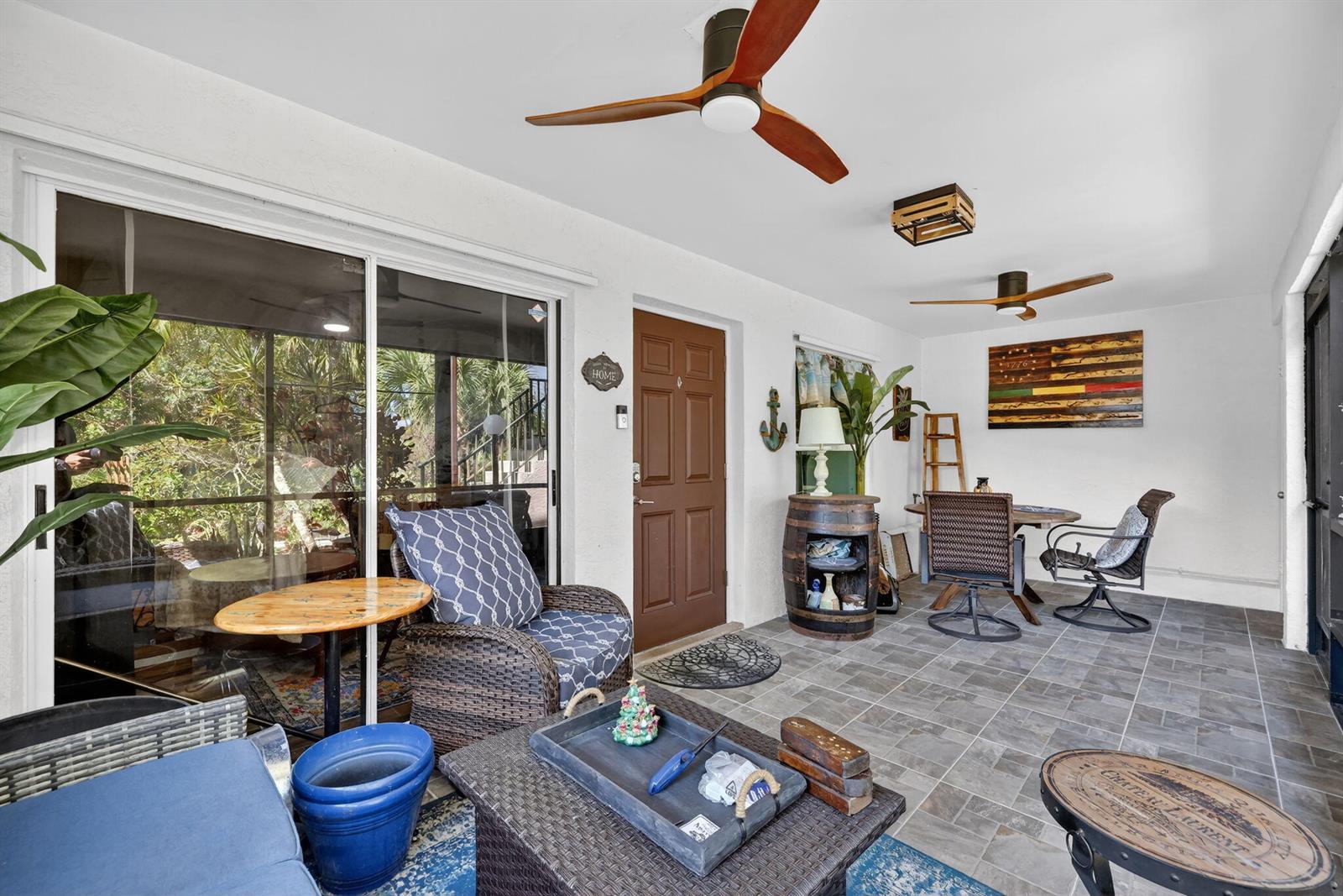 A covered patio features tiled flooring, wicker furniture, ceiling fans, and a brown entry door — 6531 SE Federal Highway # 103, Stuart FL 34997, STUART, FL