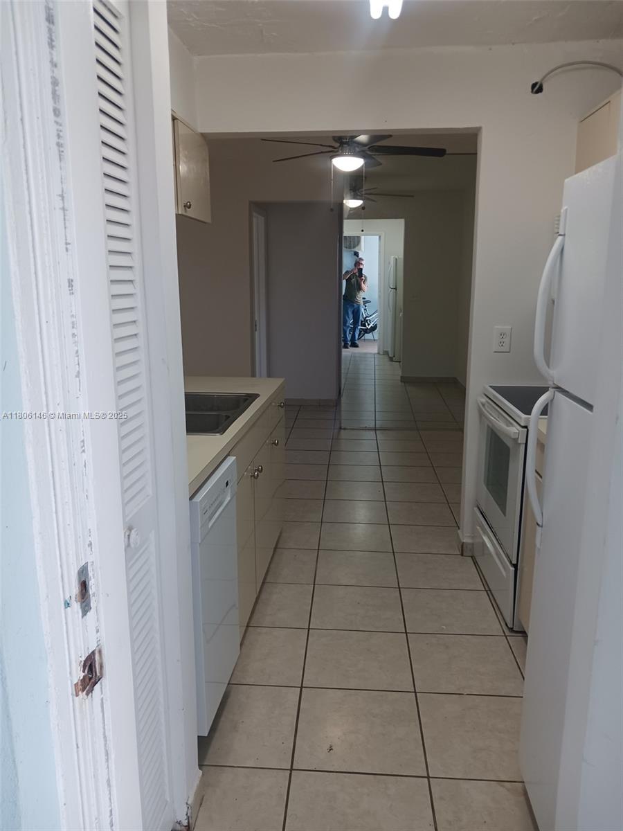 A galley-style kitchen features white appliances, light-colored cabinets, and tiled flooring — 2700 NE 135th St # 30, North Miami FL 33181, NORTH MIAMI, FL