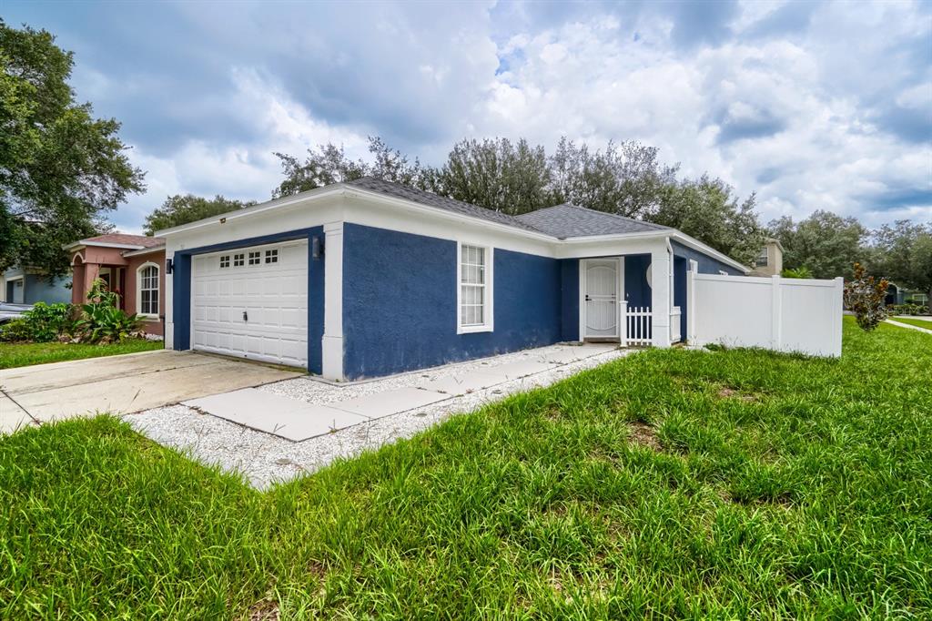 A blue single-story house with a white garage door, white trim, and a white fence — 701 PERIWINKLE POINTE PLACE, SEFFNER, FL