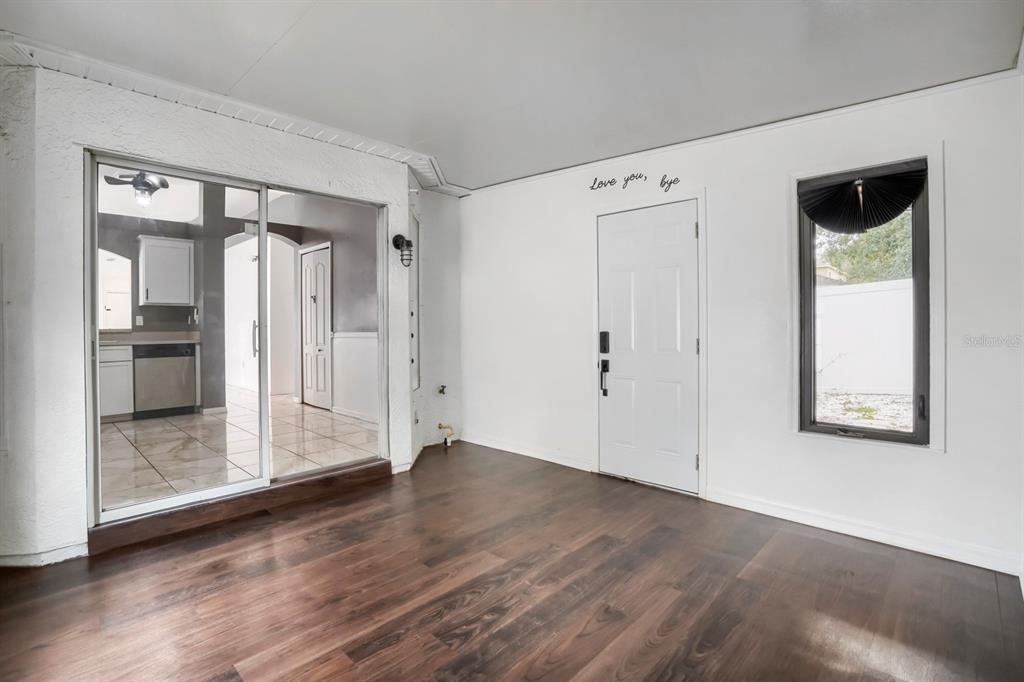 A room with dark wood-look flooring, a sliding glass door, and a white entry door — 701 PERIWINKLE POINTE PLACE, SEFFNER, FL