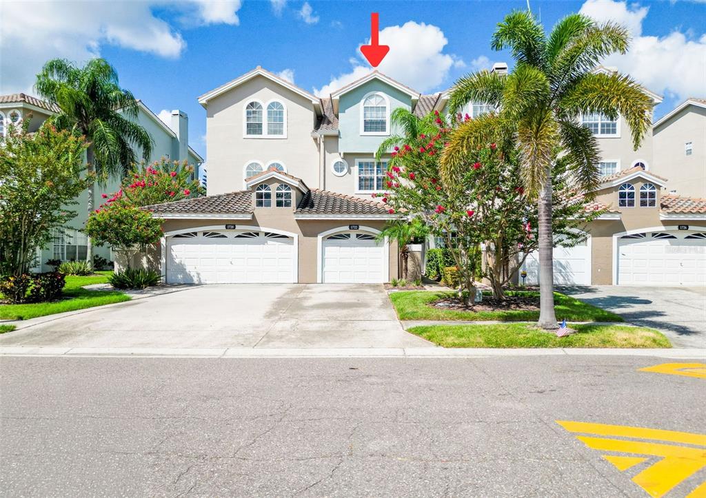 A three-story townhouse exterior features a two-car garage, light-colored stucco walls, and a red arrow — 1722 ARABIAN LANE, PALM HARBOR, FL