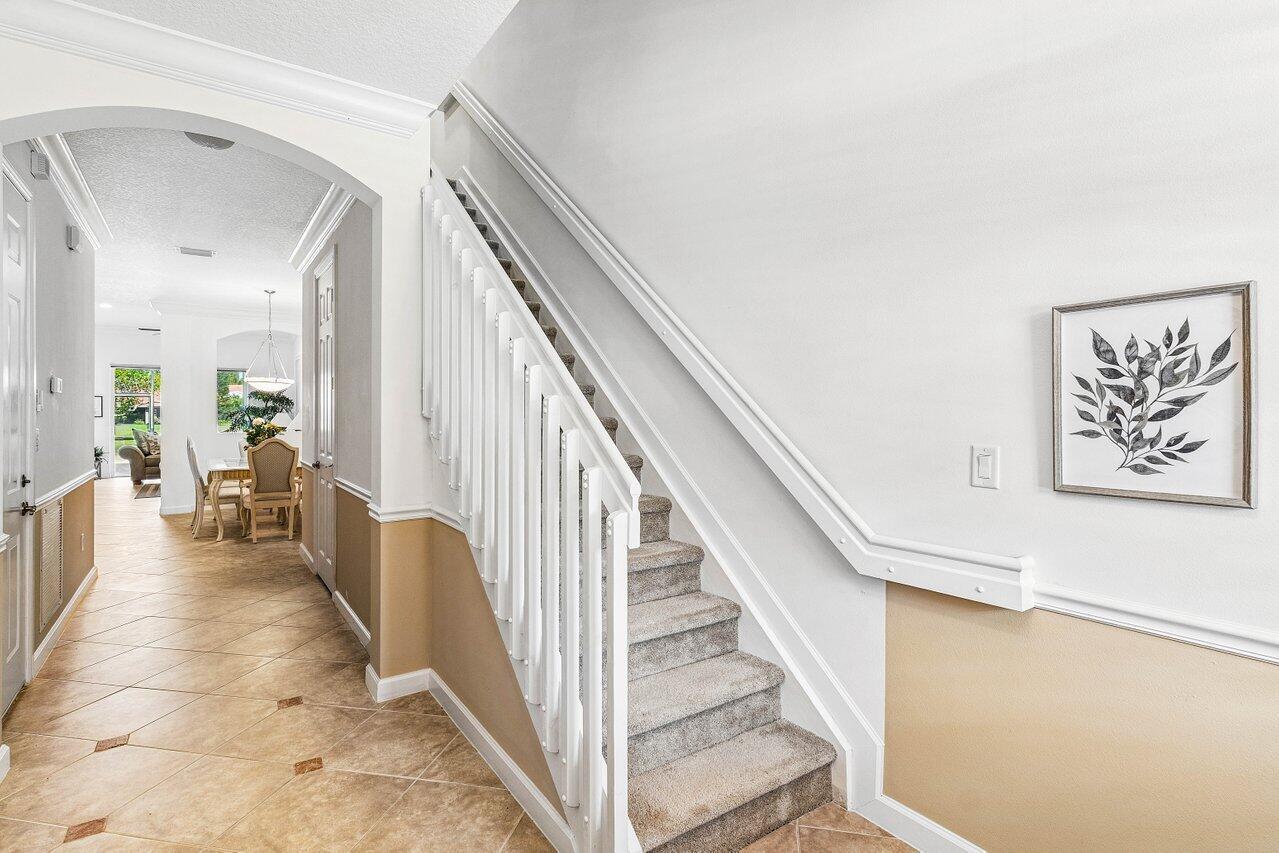 An entryway features a carpeted staircase with white railings and tile flooring leading to a dining area — 23069 Addison Lakes Circle, Boca Raton FL 33433, BOCA RATON, FL