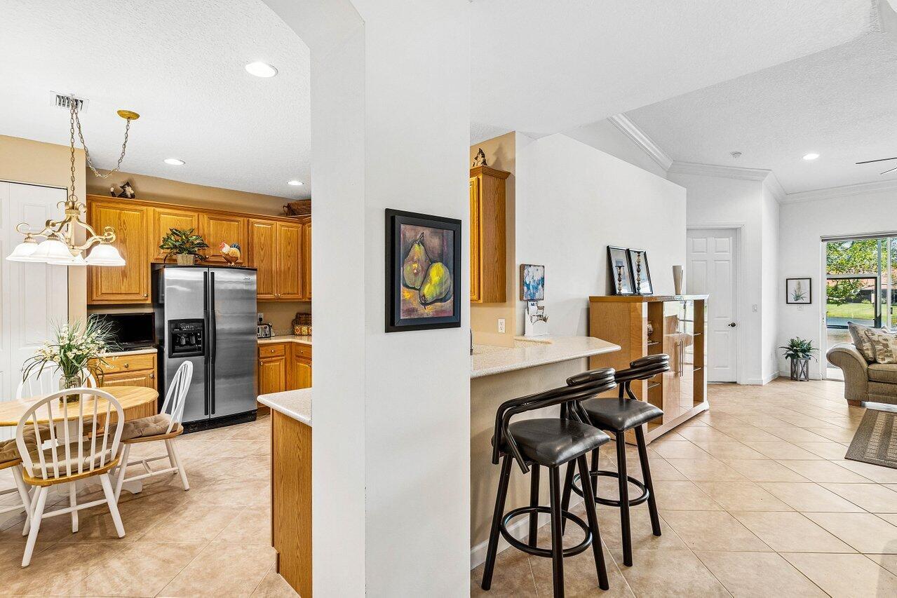 A kitchen with wood cabinets and a breakfast bar opens into a tiled living area — 23069 Addison Lakes Circle, Boca Raton FL 33433, BOCA RATON, FL