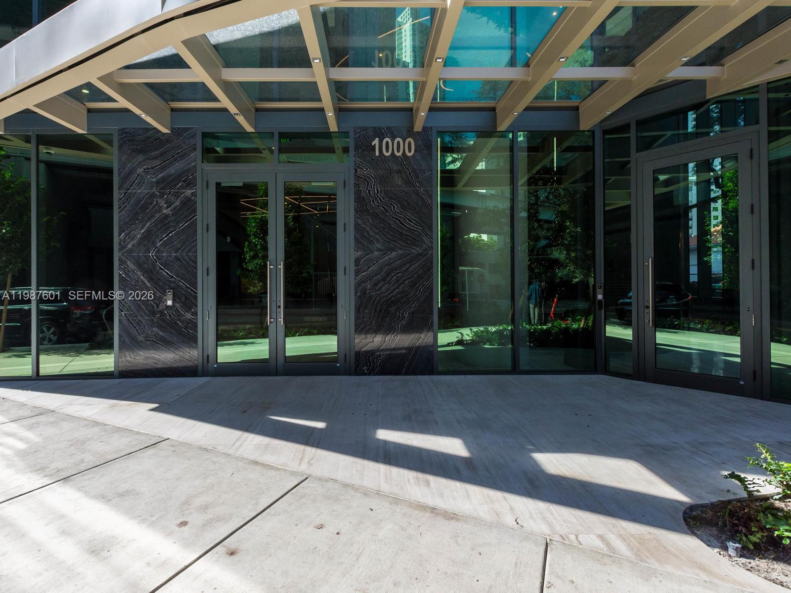 The exterior entrance of a modern building features glass doors, a stone facade, and a canopy — 1000 Brickell Plz # 4104, Miami FL 33131, MIAMI, FL
