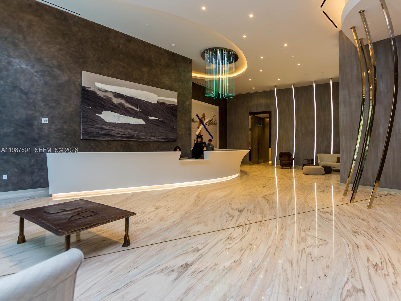 A modern lobby features a white reception desk, marble flooring, and a unique hanging light fixture — 1000 Brickell Plz # 4104, Miami FL 33131, MIAMI, FL