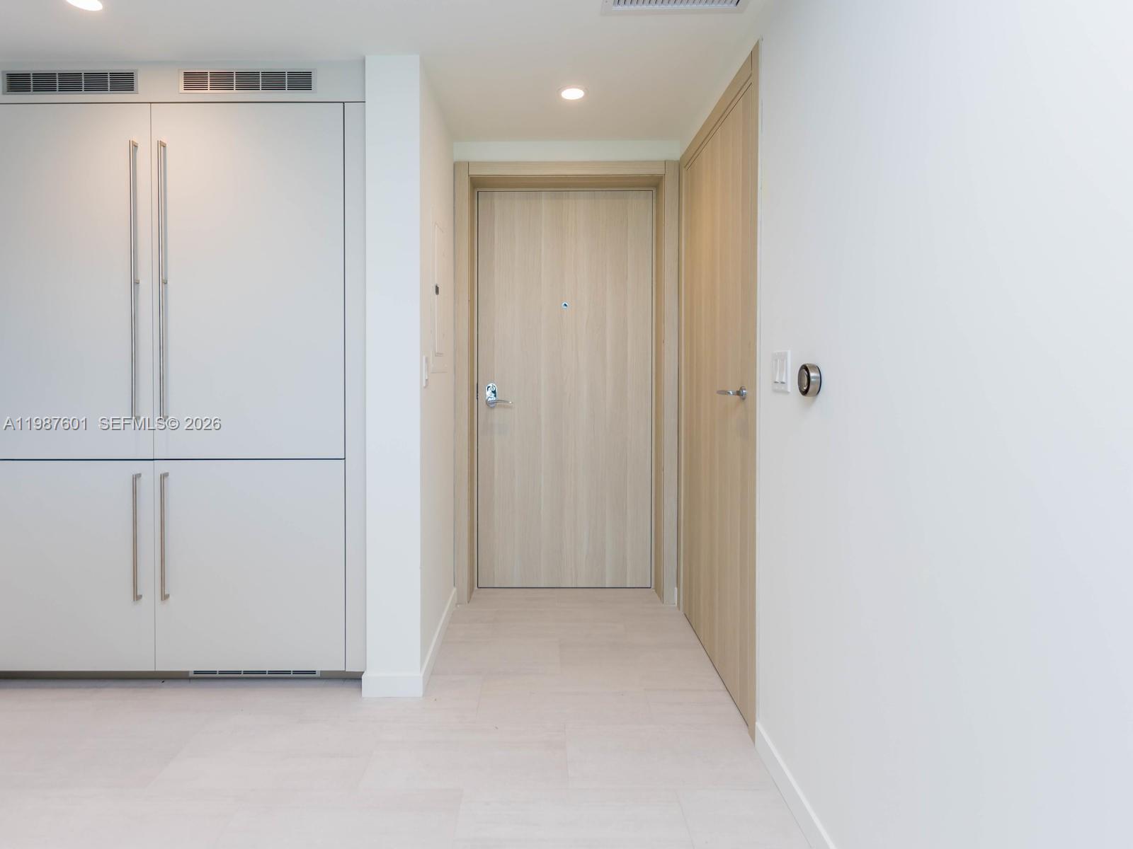 A hallway features light wood doors, white cabinetry, and a modern thermostat on the wall — 1000 Brickell Plz # 4104, Miami FL 33131, MIAMI, FL