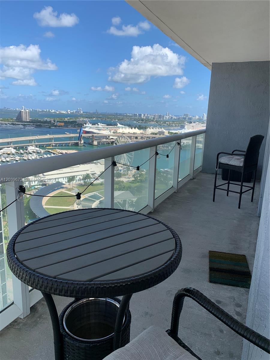 A high-rise balcony features a small table, two chairs, string lights, and a waterfront view — 50 Biscayne Blvd # 3001, Miami FL 33132, MIAMI, FL
