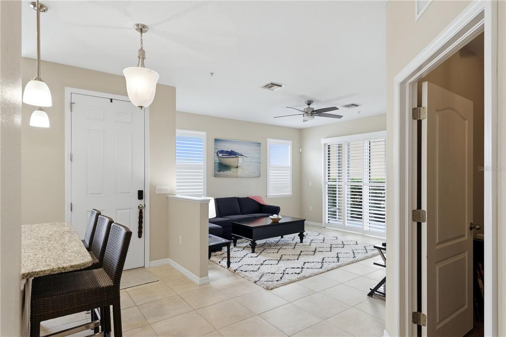 A living room with tile floors, a dark sofa, and a dining area with bar stools — 8423 KARPEAL DRIVE UNIT 1501, SARASOTA, FL