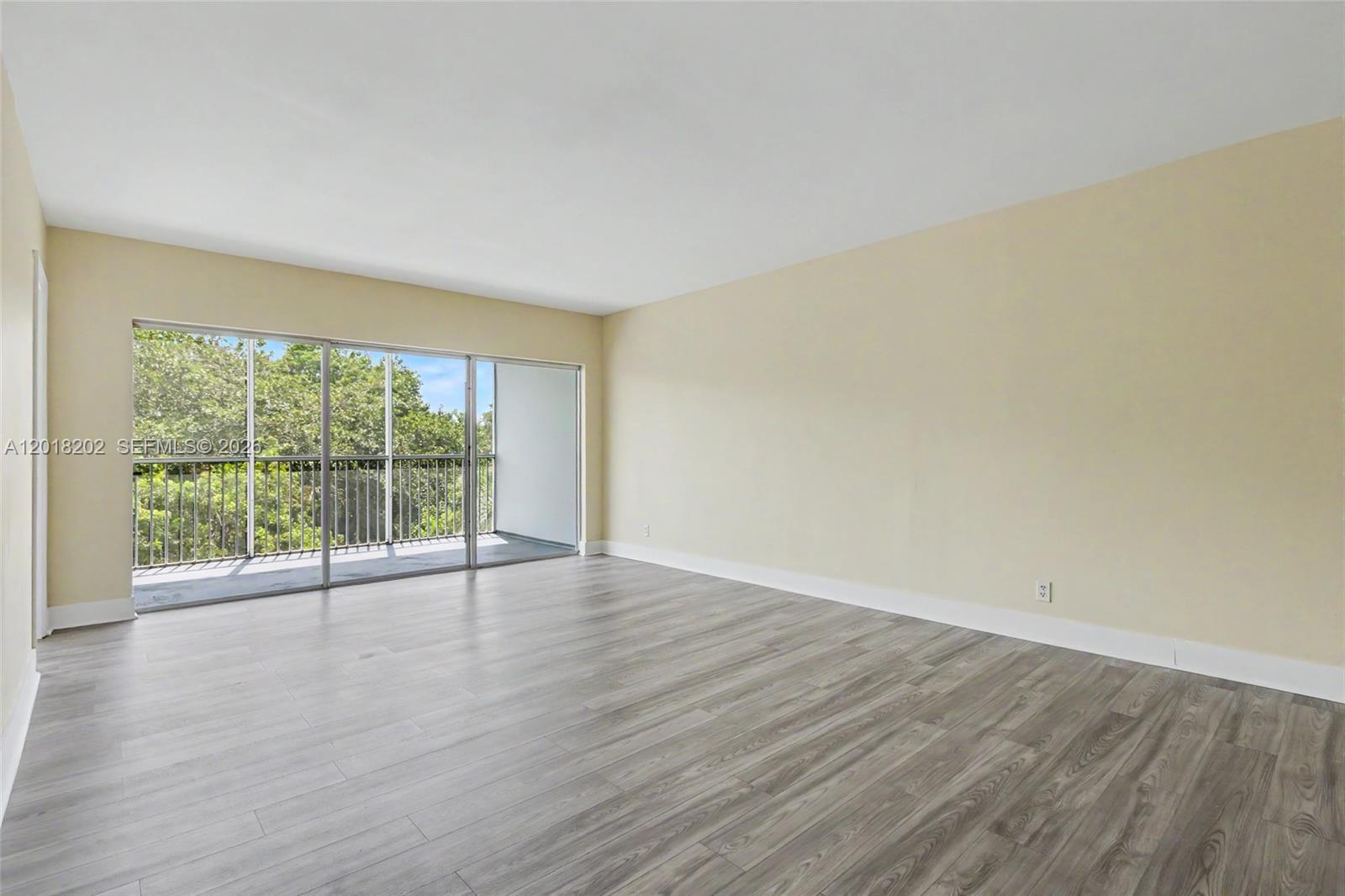 An empty room features light-colored walls, wood-look flooring, and a sliding glass door to a balcony — 3250 N Palm Aire Dr # 406, Pompano Beach FL 33069, POMPANO BEACH, FL