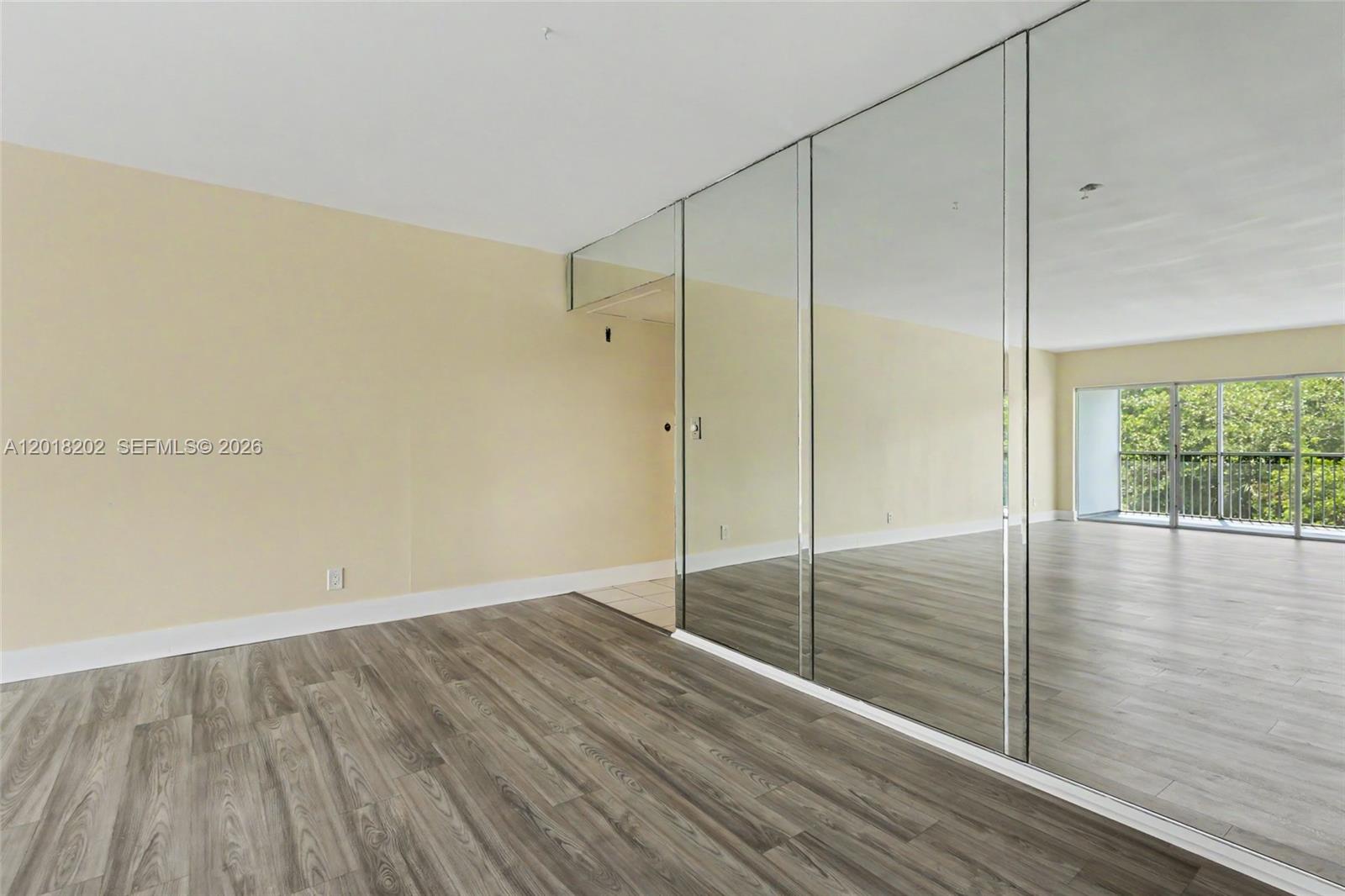 This living and dining room features neutral furniture, wood-look flooring, and a mirrored wall — 3250 N Palm Aire Dr # 406, Pompano Beach FL 33069, POMPANO BEACH, FL