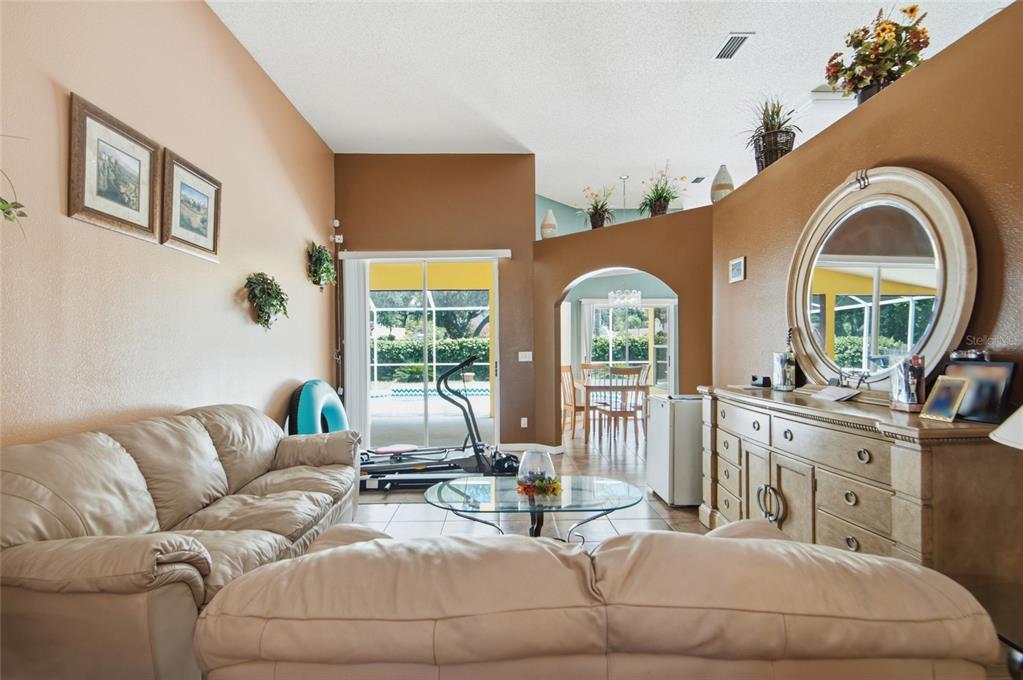 A living room with a beige sofa, glass coffee table, and a view of a pool — 9602 SUNNYOAK DRIVE, RIVERVIEW, FL