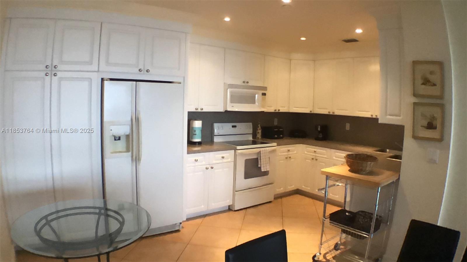 A kitchen features white cabinetry, white appliances, a glass dining table, and tile flooring — 151 Crandon Blvd # 833, Key Biscayne FL 33149, KEY BISCAYNE, FL