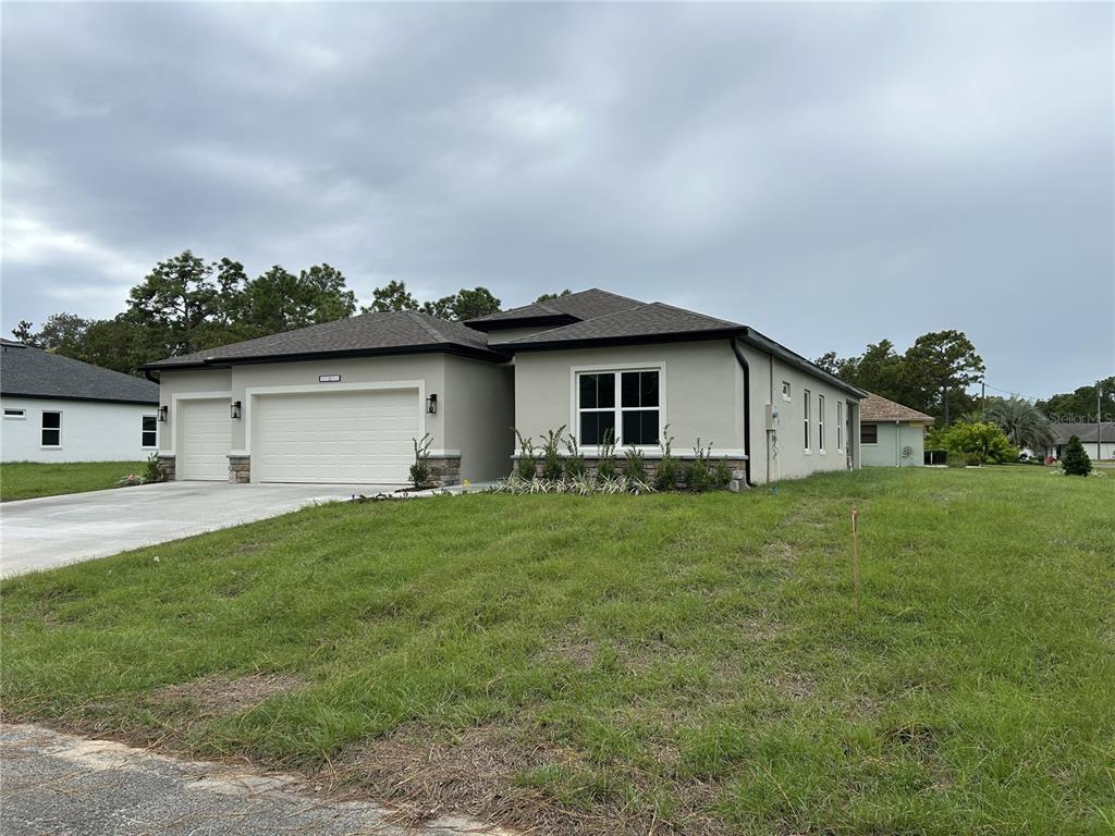 A single-story house with a beige stucco exterior, a three-car garage, and a grassy yard — 51 GRASS STREET, HOMOSASSA, FL