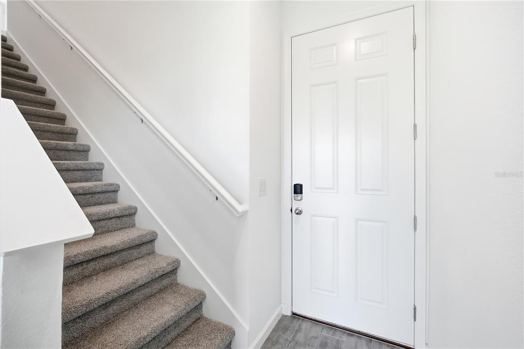 A carpeted staircase with a white handrail sits next to a white front door — 2419 29TH LANE E, PALMETTO, FL