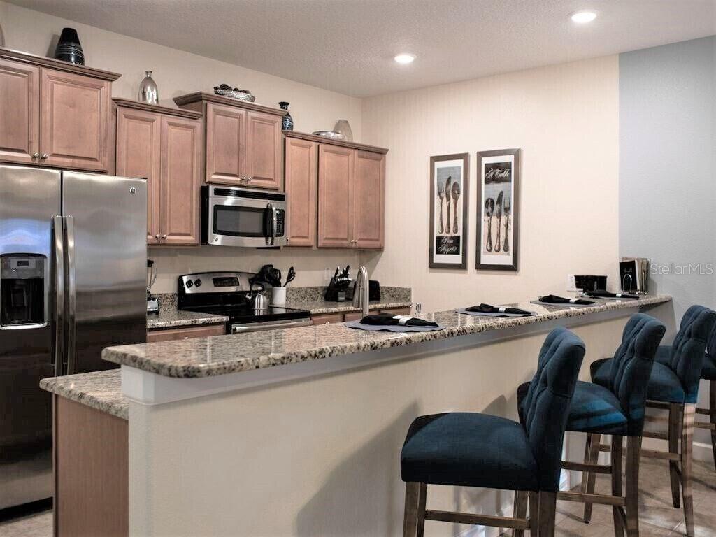 A kitchen with wood cabinets, granite countertops, stainless steel appliances, and a breakfast bar — 2945 BANANA PALM DRIVE, KISSIMMEE, FL