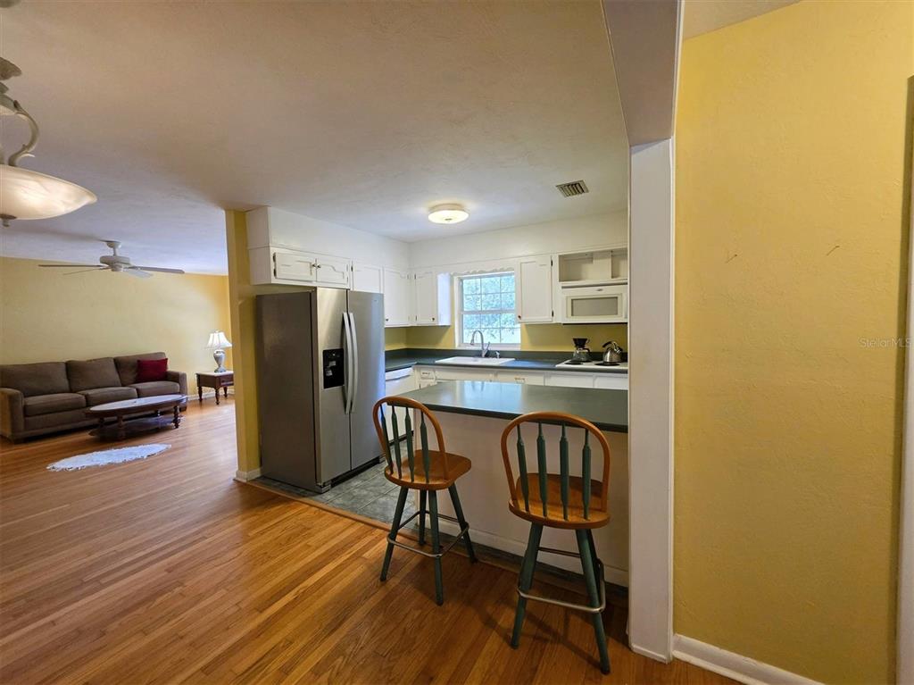 A kitchen with white cabinets and a breakfast bar overlooks a living room area — 735 OVERHILL ROAD, DELAND, FL