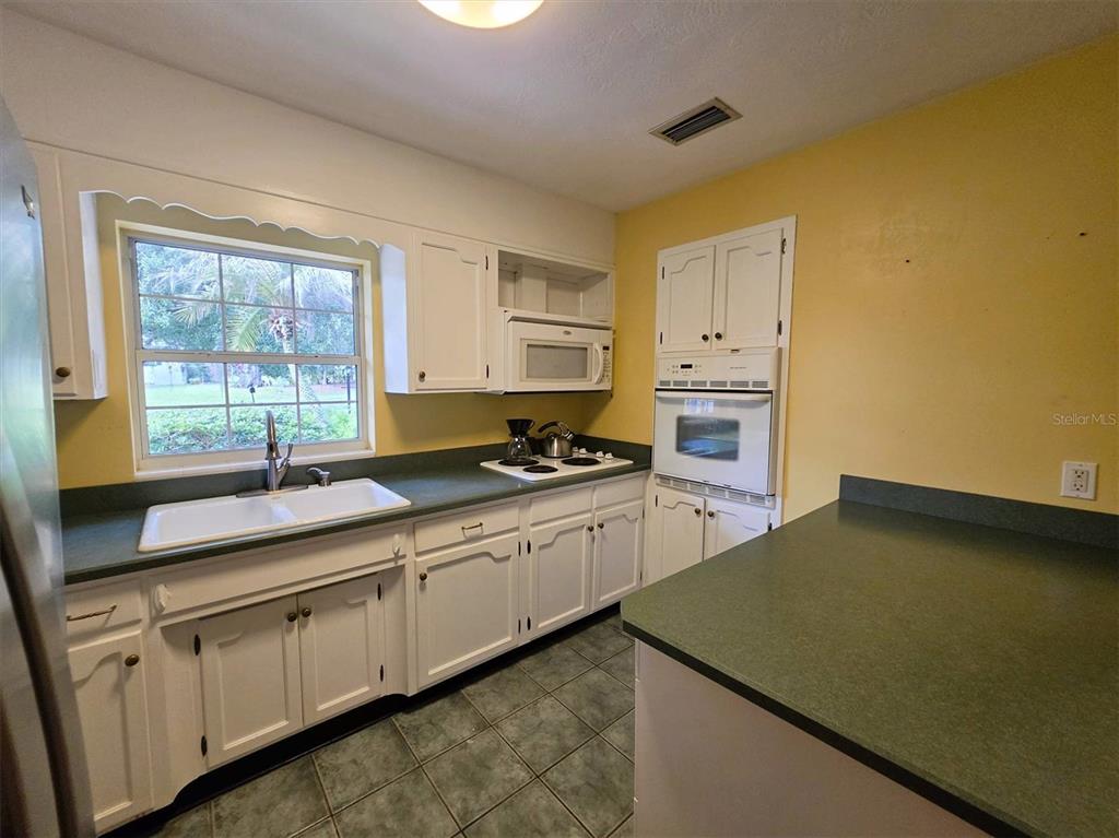 A kitchen features white cabinets, green countertops, a double sink, and a wall-mounted oven — 735 OVERHILL ROAD, DELAND, FL