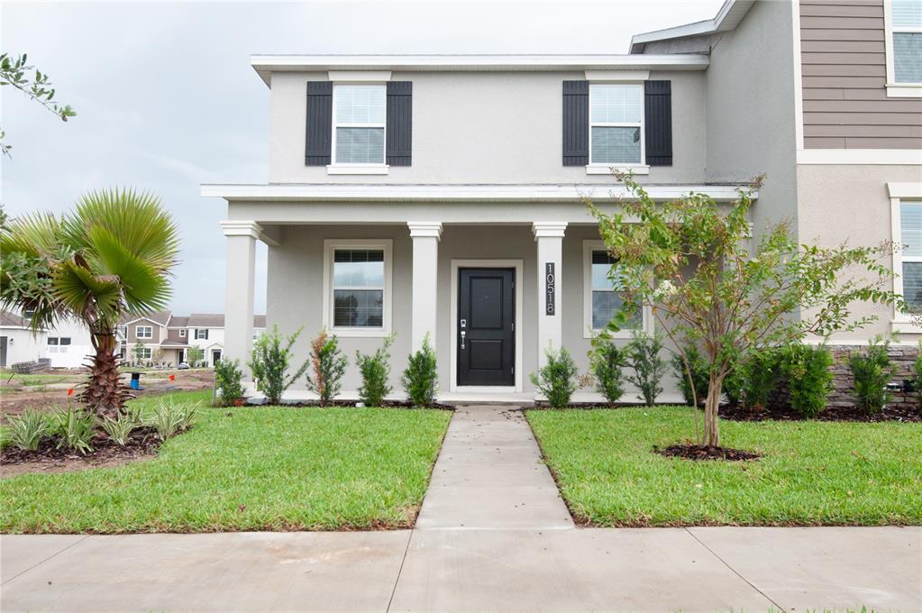A two-story house features a covered front porch, a black door, and a landscaped lawn — 10518 TRIBUTE DRIVE, WINTER GARDEN, FL