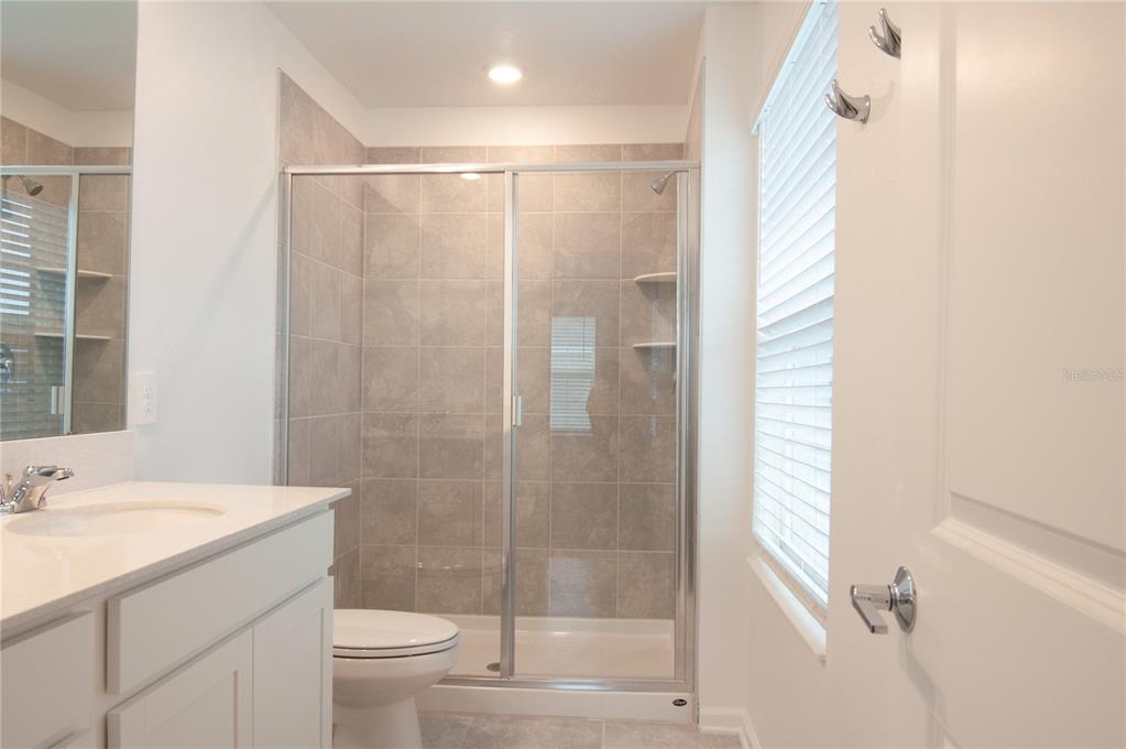 A bathroom features a white vanity, a tiled walk-in shower, and a toilet — 10518 TRIBUTE DRIVE, WINTER GARDEN, FL