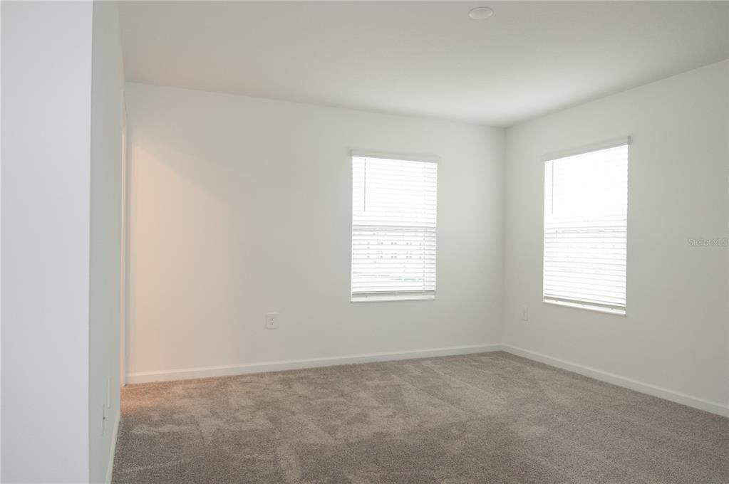 An empty bedroom features white walls, gray carpeting, and two windows with white blinds — 10518 TRIBUTE DRIVE, WINTER GARDEN, FL
