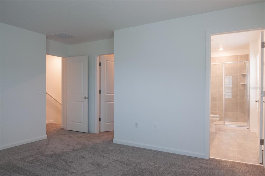 A carpeted bedroom features two closed interior doors and an open doorway to a bathroom — 10518 TRIBUTE DRIVE, WINTER GARDEN, FL