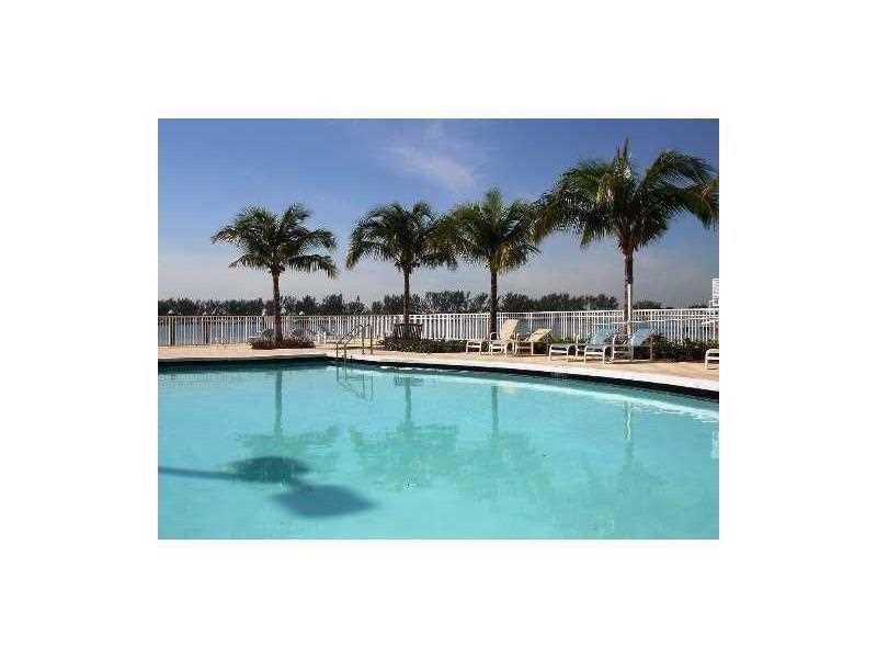 A swimming pool with lounge chairs and palm trees overlooks a white fence and water — 2101 Brickell Avenue # 808, Miami FL 33129, MIAMI, FL