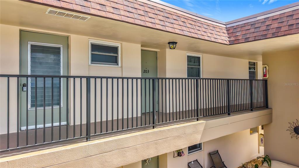 An exterior view of a second-story apartment walkway with a black railing and unit 203 — 9945 47TH AVENUE N UNIT 203, ST PETERSBURG, FL