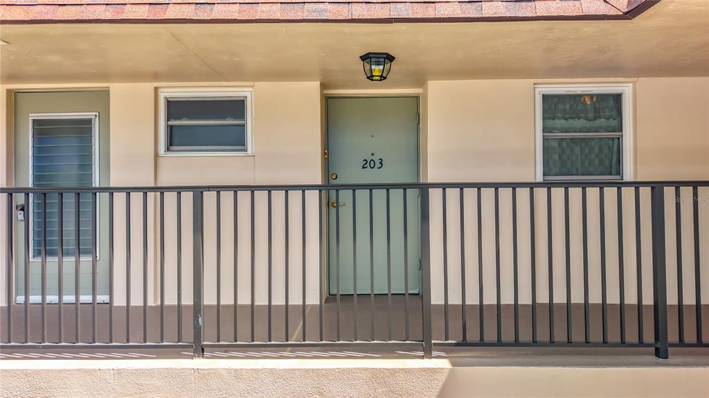 An exterior view of a building entrance with a numbered door and metal railing — 9945 47TH AVENUE N UNIT 203, ST PETERSBURG, FL