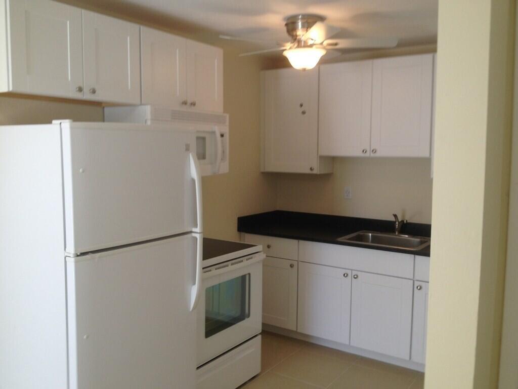 A kitchen features white cabinets, a black countertop, white appliances, and a ceiling fan — 203 SE 4th Avenue, Boynton Beach FL 33435, BOYNTON BEACH, FL