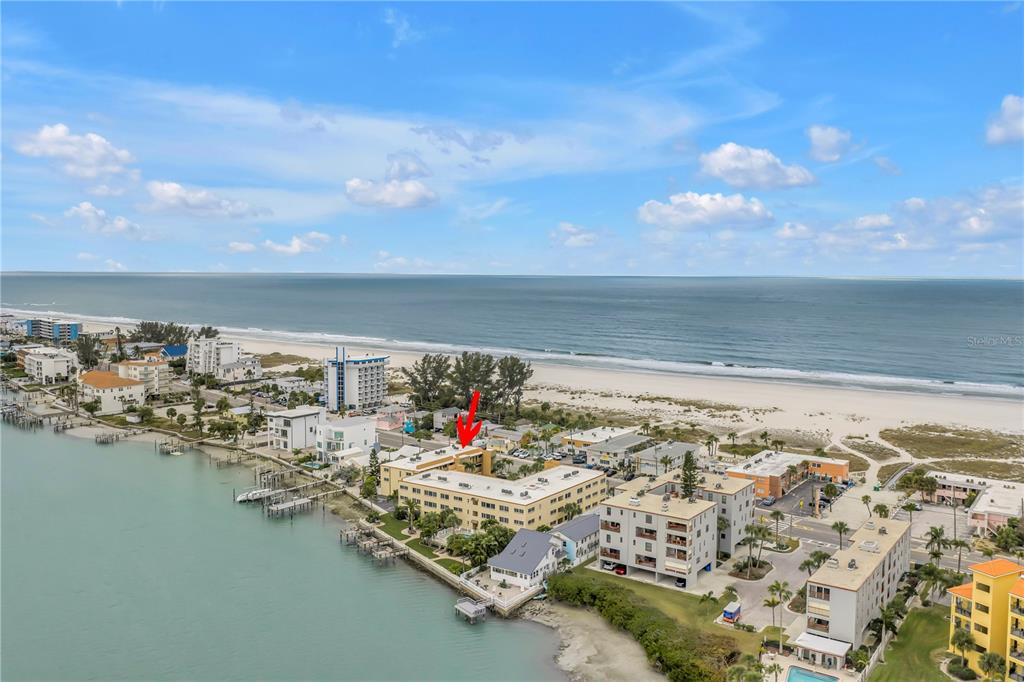 An aerial view shows a multi-story apartment building located between a bay and the ocean — 10265 GULF BOULEVARD UNIT B315, ST PETERSBURG, FL