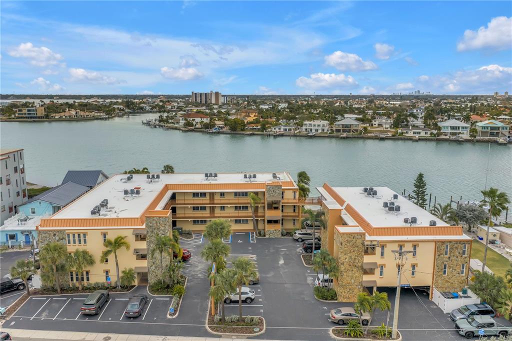An aerial view shows a multi-story apartment building with a parking lot and waterfront access — 10265 GULF BOULEVARD UNIT B315, ST PETERSBURG, FL