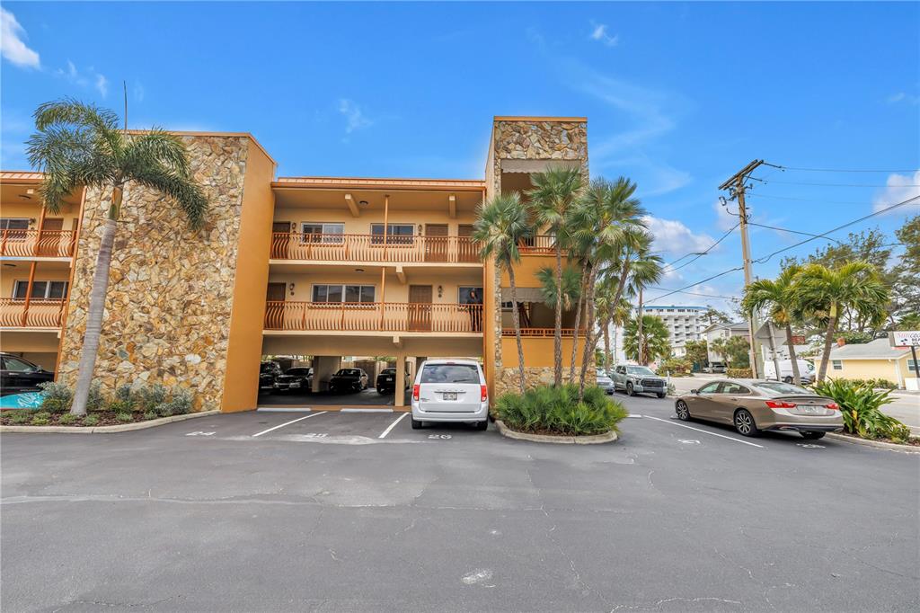 A three-story building with stone accents, balconies, and a ground-level parking area — 10265 GULF BOULEVARD UNIT B315, ST PETERSBURG, FL