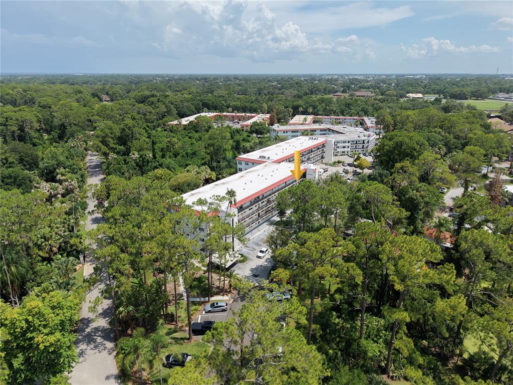 An aerial view shows a multi-story apartment building surrounded by trees and a parking lot — 200 EL CAMINO DRIVE UNIT 306, WINTER HAVEN, FL