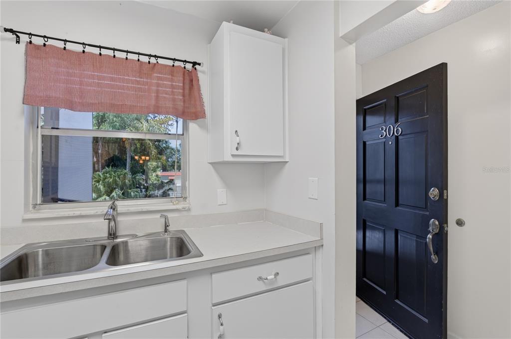 A kitchen sink area features white cabinets, a window with a valance, and a black door — 200 EL CAMINO DRIVE UNIT 306, WINTER HAVEN, FL