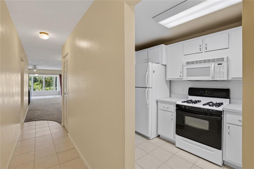 A tiled hallway leads to a kitchen with white cabinets and appliances next to a living area — 200 EL CAMINO DRIVE UNIT 306, WINTER HAVEN, FL