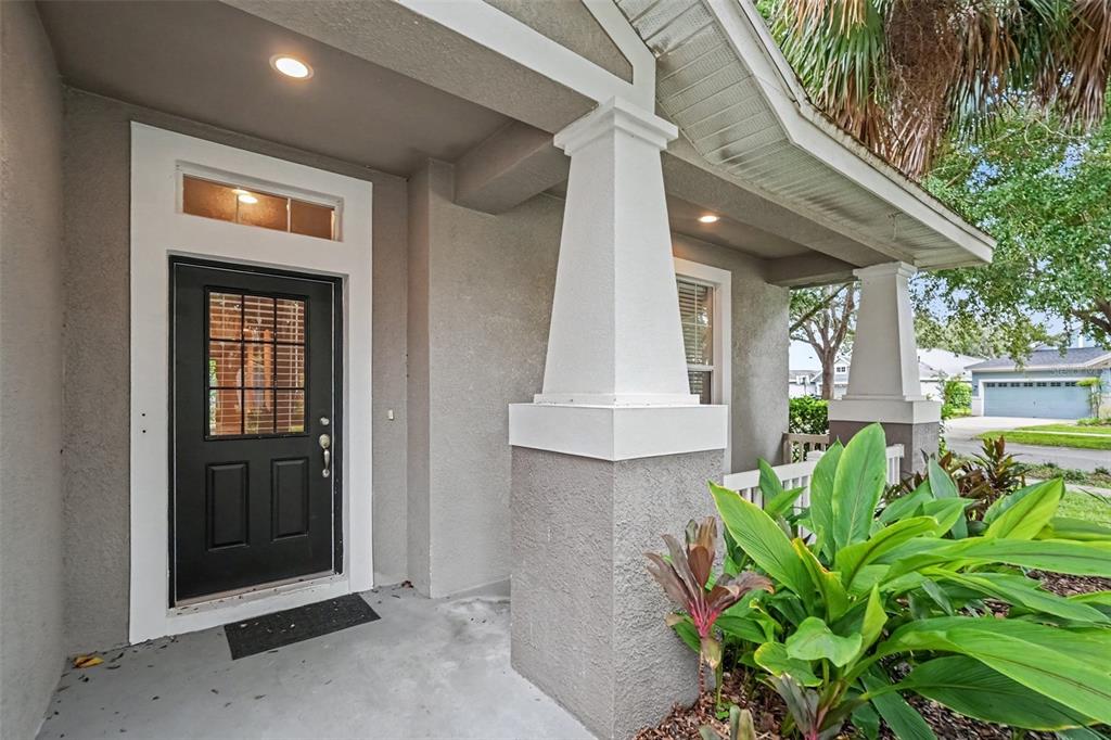 A covered front porch features a black door, white columns, and a small garden bed — 15536 GANNETGLADE LANE, LITHIA, FL