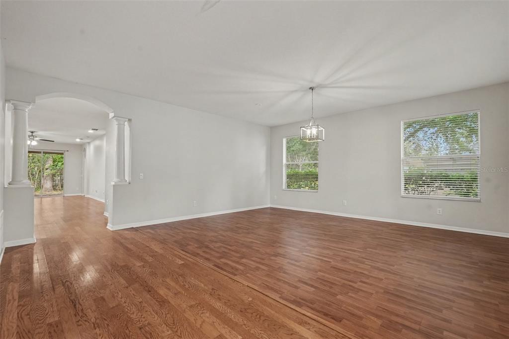 An empty living room features hardwood floors, white walls, and an arched entryway with columns — 15536 GANNETGLADE LANE, LITHIA, FL