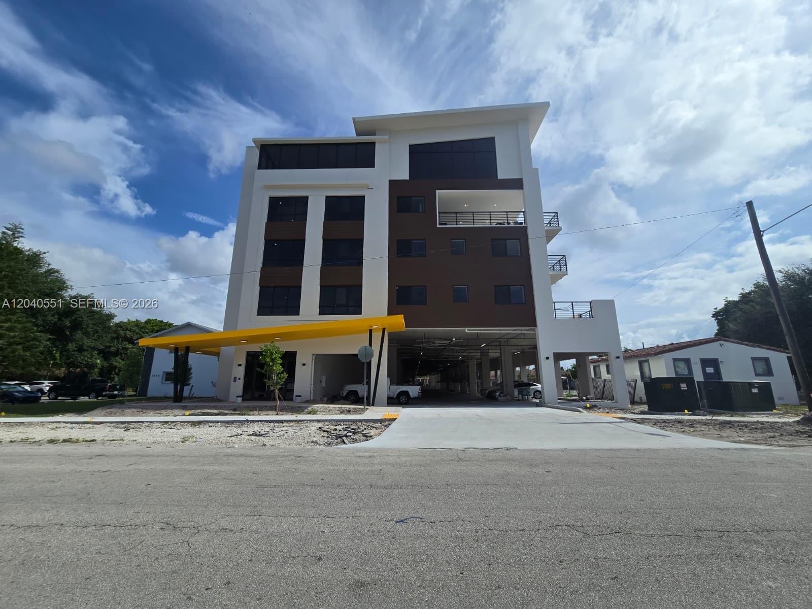 A modern multi-story building features a yellow canopy, ground-level parking, and dark brown accents — 2233 Fillmore St # 402, Hollywood FL 33020, HOLLYWOOD, FL