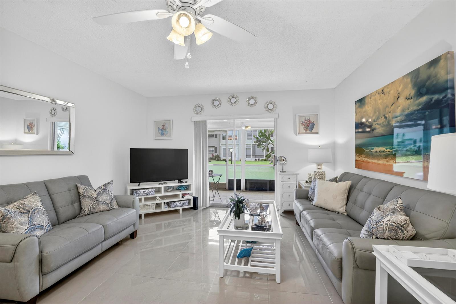 A living room features two gray sofas, a white coffee table, and a sliding glass door — 5681 SW 2nd Court # 106, Margate FL 33068, MARGATE, FL