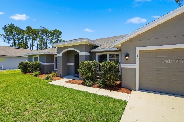 A gray single-story house features a concrete driveway, a front entryway, and landscaped bushes — 55 BENNETT LANE, PALM COAST, FL