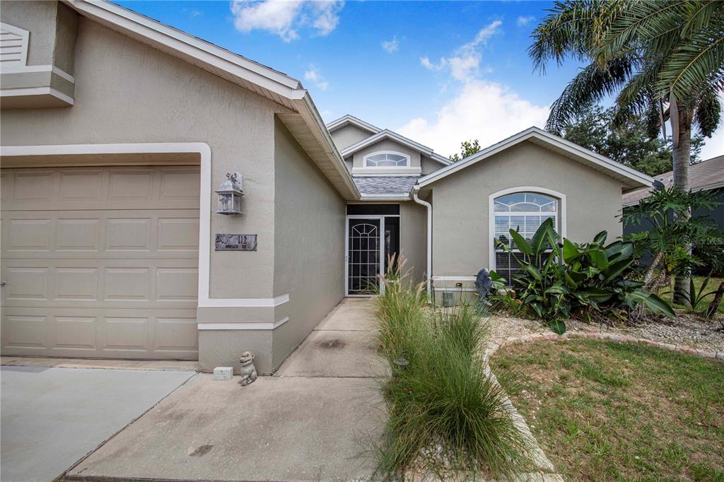 A single-story house exterior features a beige stucco facade, a garage, and a front walkway — 112 MONACO DRIVE, DAVENPORT, FL