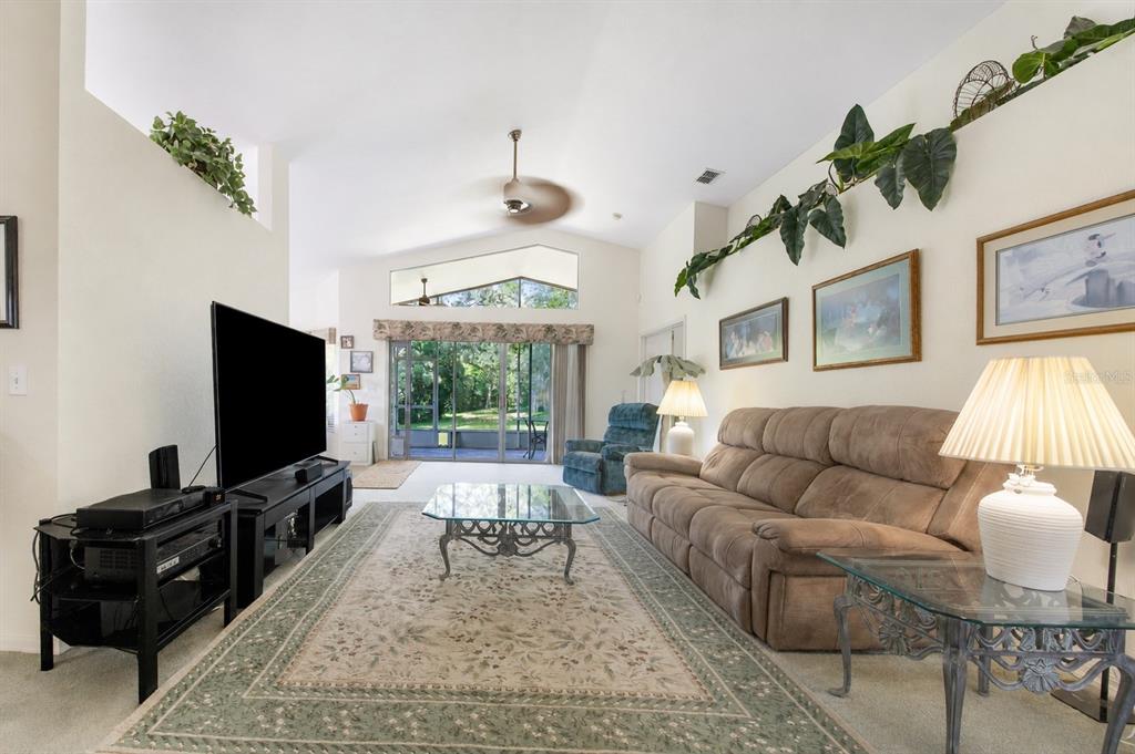 A living room with a vaulted ceiling, a brown sofa, and a glass-topped coffee table — 112 MONACO DRIVE, DAVENPORT, FL