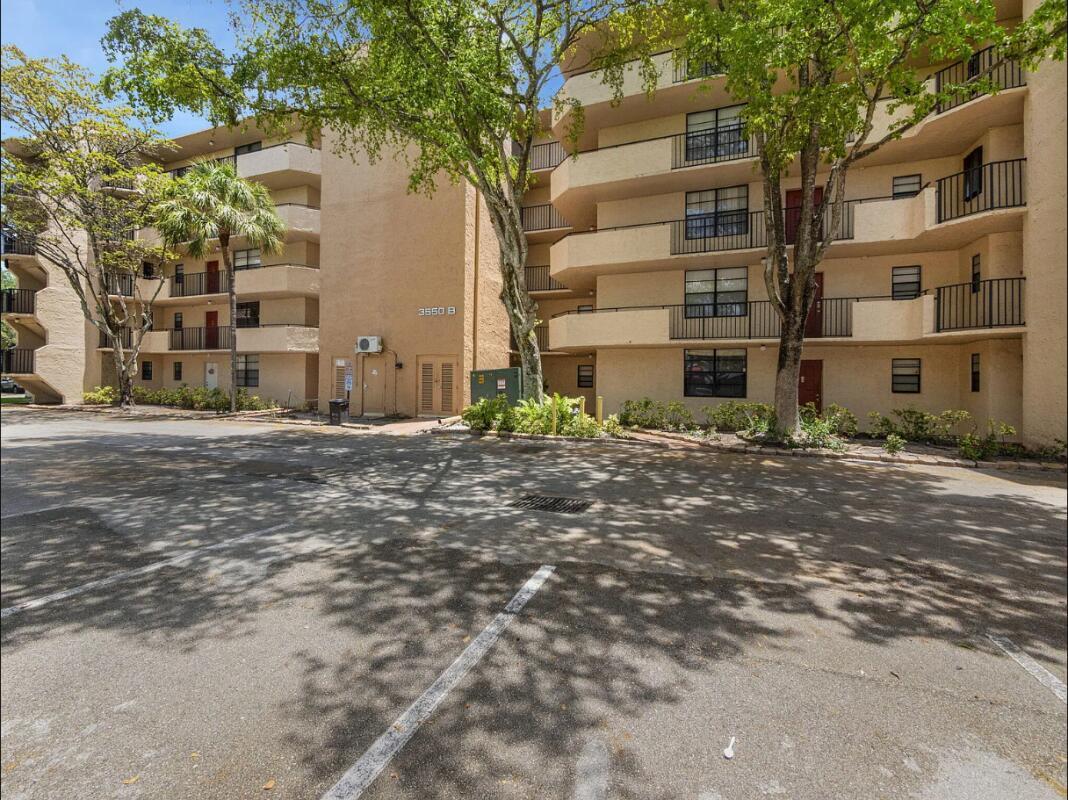 A multi-story apartment building with tan stucco walls, balconies, and a paved parking lot — 3550 Blue Lake Drive # 404, Pompano Beach FL 33064, POMPANO BEACH, FL