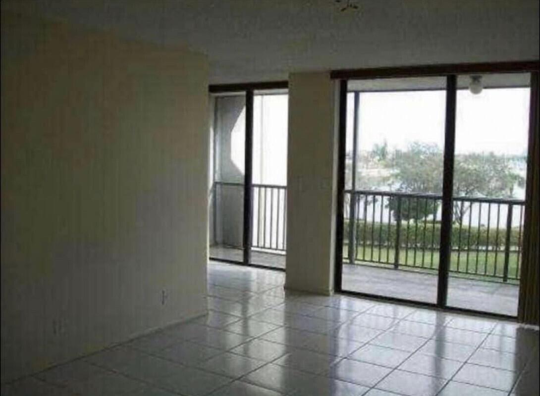 An empty room with light-colored tile flooring and large sliding glass doors leading to balconies — 3550 Blue Lake Drive # 404, Pompano Beach FL 33064, POMPANO BEACH, FL