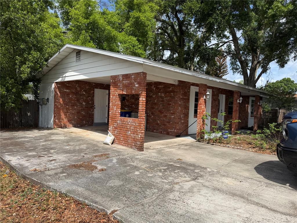 A single-story brick house with a carport and a concrete driveway under large trees — 415 S TANGERINE COURT, EAGLE LAKE, FL