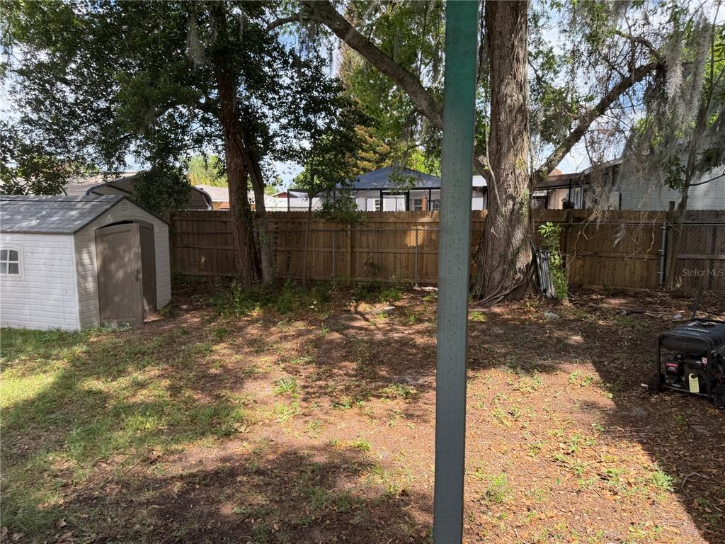A backyard features a storage shed, a wooden fence, and several large trees — 415 S TANGERINE COURT, EAGLE LAKE, FL