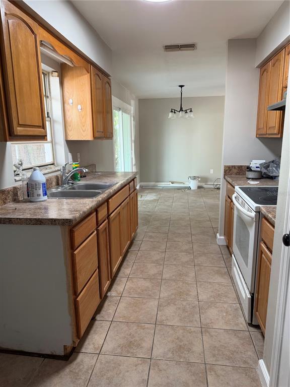A galley kitchen features oak cabinets, laminate countertops, and tile flooring leading to a dining area — 415 S TANGERINE COURT, EAGLE LAKE, FL