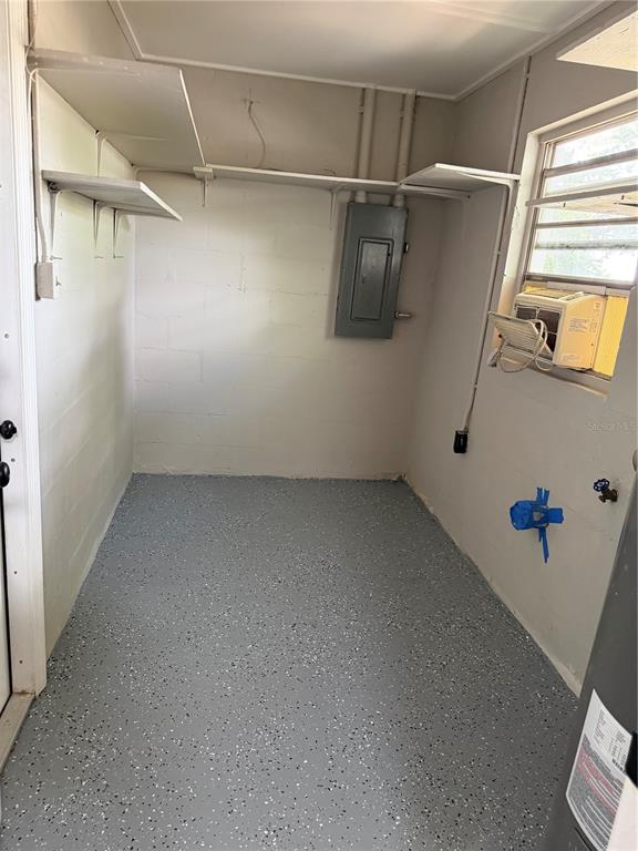 A utility room with gray speckled flooring, white block walls, open shelving, and an electrical panel — 415 S TANGERINE COURT, EAGLE LAKE, FL